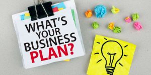 Foglio con scritta "what's your business Plan?" affiancato da un foglio giallo con il disegno di una lampadina