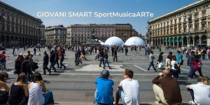 Giovani ed altra gente a passeggio in piazza Duomo a Milano, con in sovrimpressione il titolo GIOVANI SMART (SportMusicaARTe)