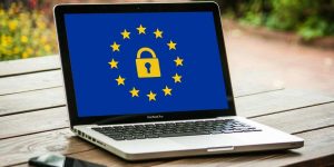 MacBook poggiato su un tavolo in esterno con sul video l'immagine di una bandiera UE con al centro un lucchetto a simbolo del GDPR