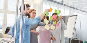 Insieme si persone che lavorano ad una lavagna trasparente con dei post-it