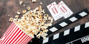 Bicchiere con popcorn versato su un tavolo con sopra il ciak per i film e 2 biglietti cinematografici