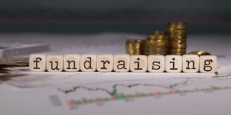 Parola "fundraising" composta da vari blocchi davanti due pile di monete e sopra dei fogli con grafici